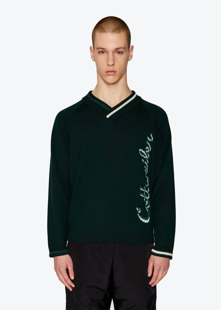 An online model wearing a green sweater and black pants.